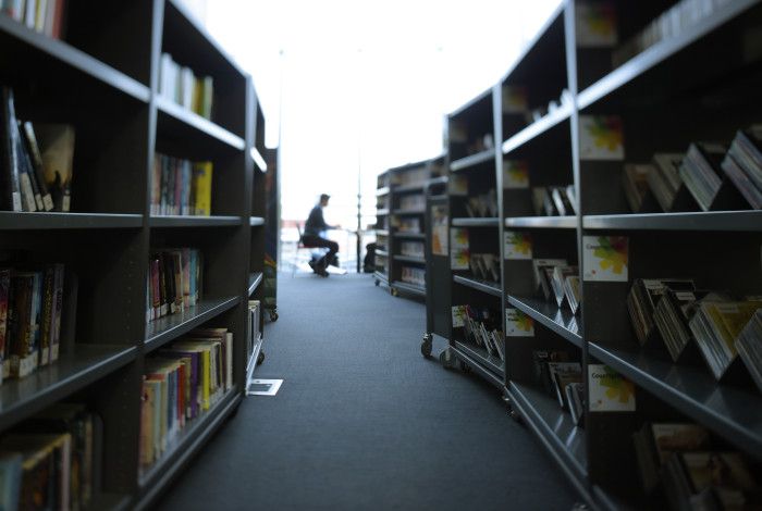 Image: Man sitting reading in a library, with bookshelves in the foreground.