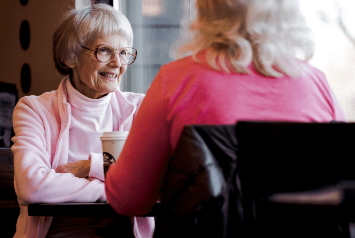 Two older women sitting at a table and chatting over a cup of coffee.