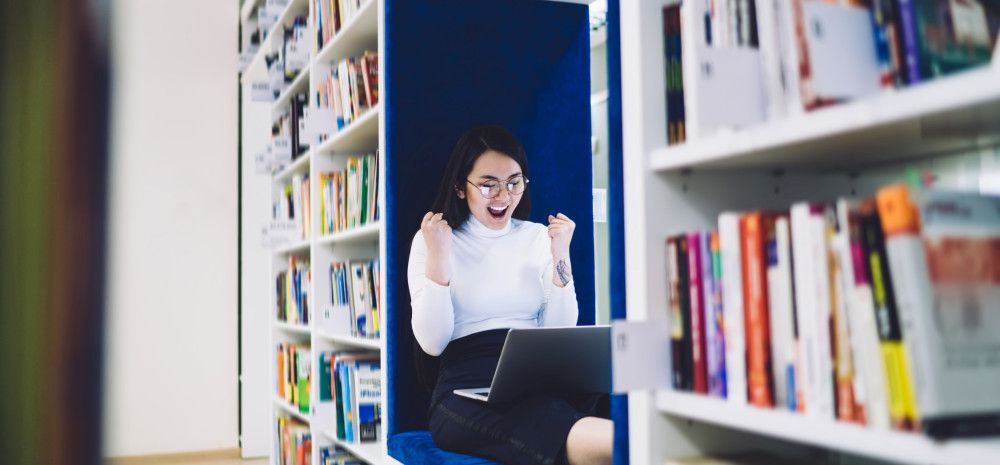 Happy student with laptop in the library.