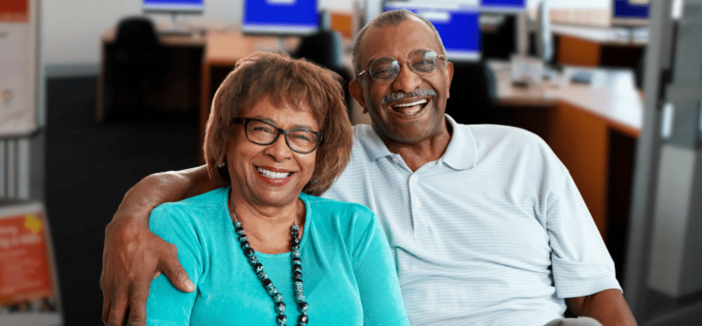 A man with his arm around a womans shoulders, both smiling at the camera.