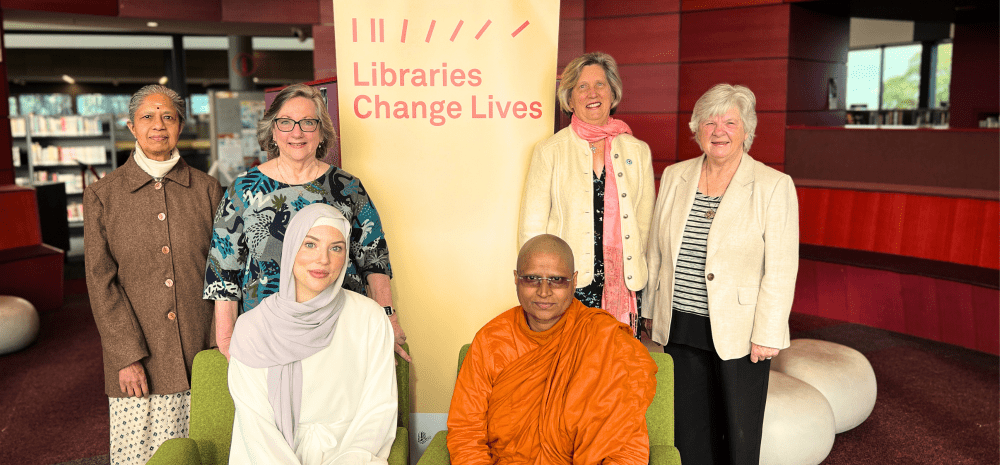 A group of women belonging to different faiths posing together for a photo in the library.