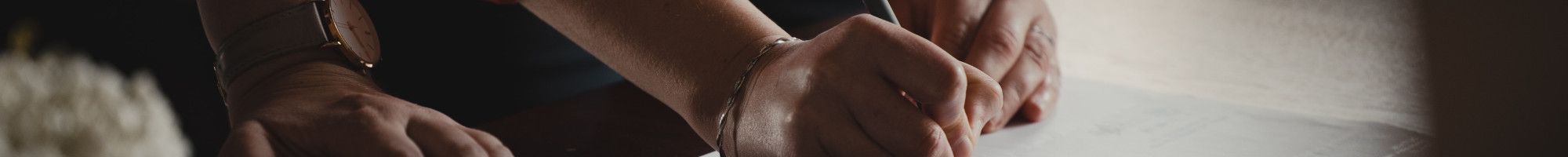 Image: view of arms and hands of two people signing documents.