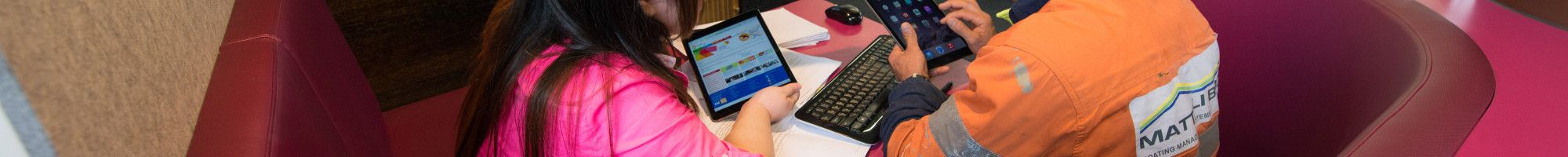 Image: a staff member helping a person use a device in the library.
