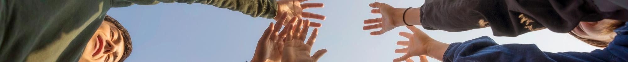 Multicultural group of people, standing in circle and raising their hands to the sky