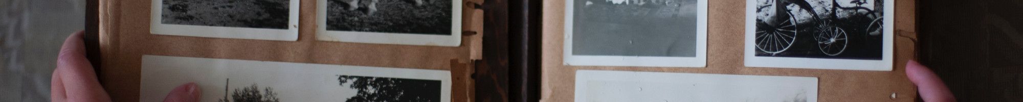 A person holding up a photo album with old black and white photos.