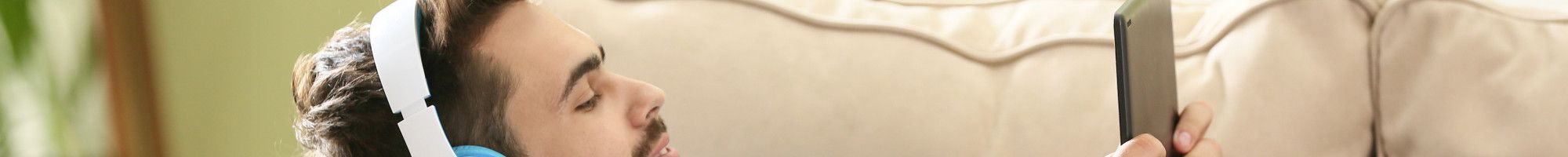 Man lying on a couch listening on headphones holding a mobile device.